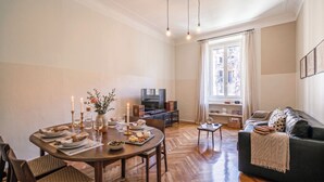Un coin repas avec une table dressée pour deux personnes, un téléviseur et un canapé offrant une vue sur la ville.