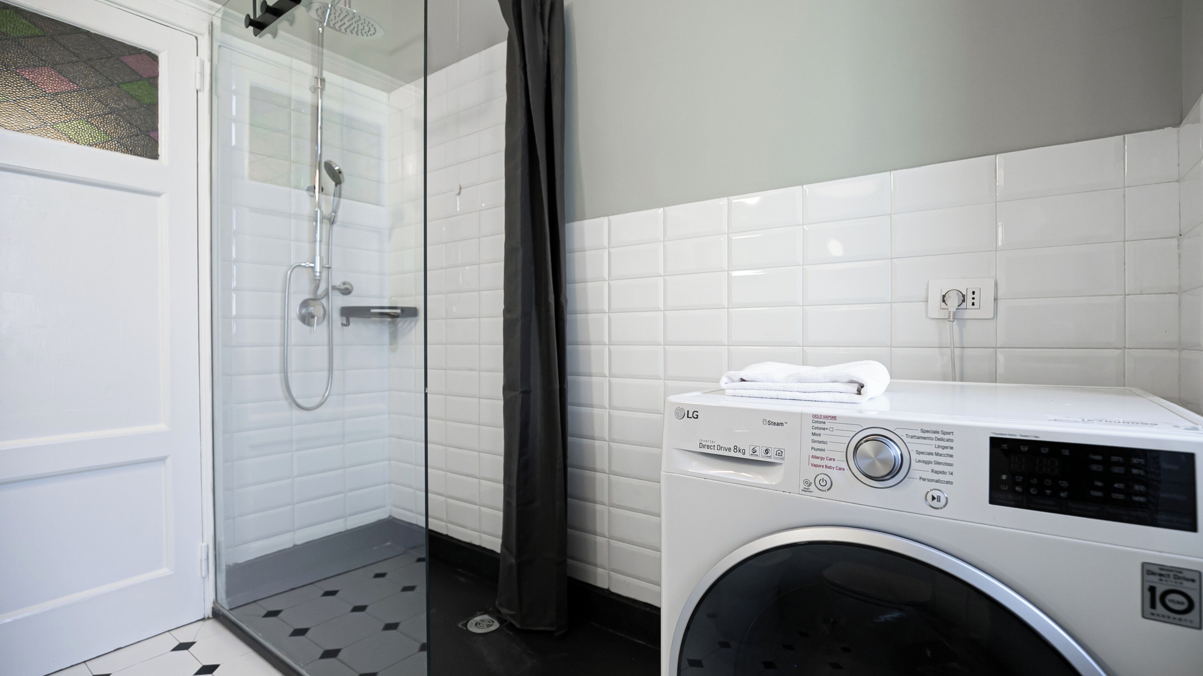 Un baño con ducha, lavadora y piso de baldosas.