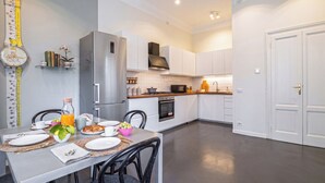 Une cuisine moderne avec des meubles blancs, des appareils en acier inoxydable et un coin repas avec une table mise pour deux personnes.