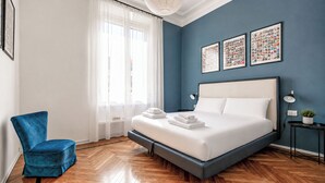 Une chambre à coucher avec un lit, une chaise, une fenêtre avec des rideaux et des œuvres d’art murales.