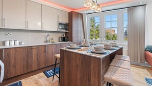 A modern kitchen with wooden cabinets, a central island, and a dining area with a bench. - Elegant 2BR flat near Waterloo Station| Big Ben | London Eye (London)