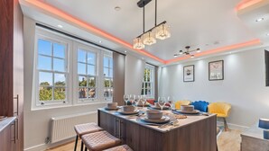 A modern kitchen with a central island, bar stools, and a dining area with a yellow chair. - Elegant 2BR flat near Waterloo Station| Big Ben | London Eye (London)