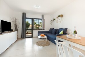 A modern living room with a TV, sofa, dining table, and a view through a large window.