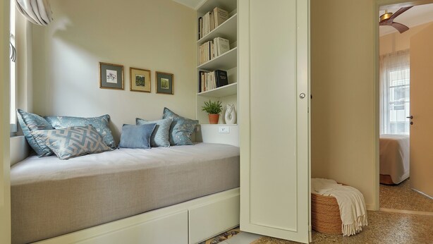 A bedroom with a bed, a bookshelf, and a door leading to another room.