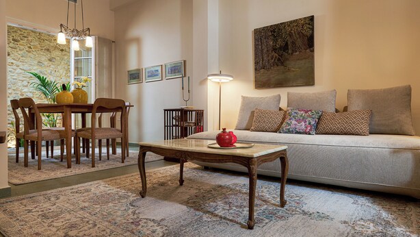 Een woonkamer met een bank, een eettafel met stoelen, een bijzettafeltje, een lamp en een schilderij aan de muur.
