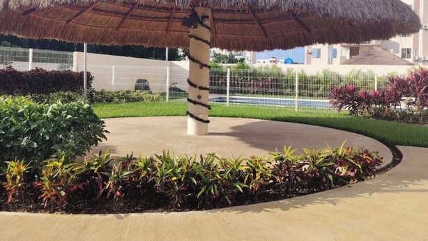 A thatched umbrella structure with a concrete base, surrounded by a landscaped garden with various plants. - Cancun apartment with pool, AC and Pet Friendly (Cancún)