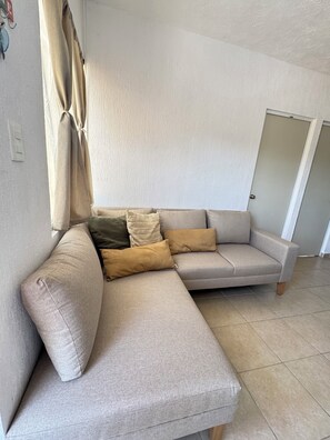 Un salon d’angle avec un canapé d’angle beige, une porte et un mur de couleur claire.