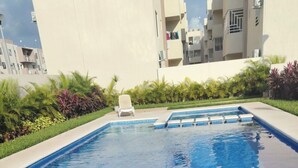 A rectangular swimming pool with a white lounge chair and a small deck area. - Cancun apartment with pool, AC and Pet Friendly (Cancún)