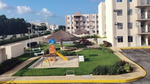 A residential area with apartment buildings, a playground, and a clear sky. - Cancun apartment with pool, AC and Pet Friendly (Cancún)