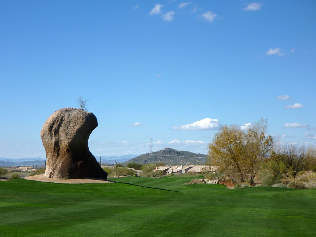 A golf course with a prominent rock formation, a clear sky, and distant mountains.