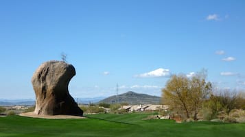 A golf course with a prominent rock formation, a clear sky, and distant mountains.