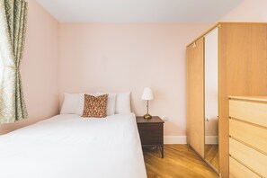 Een slaapkamer met een bed, kussens, een nachtkastje, een lamp en een kledingkast.