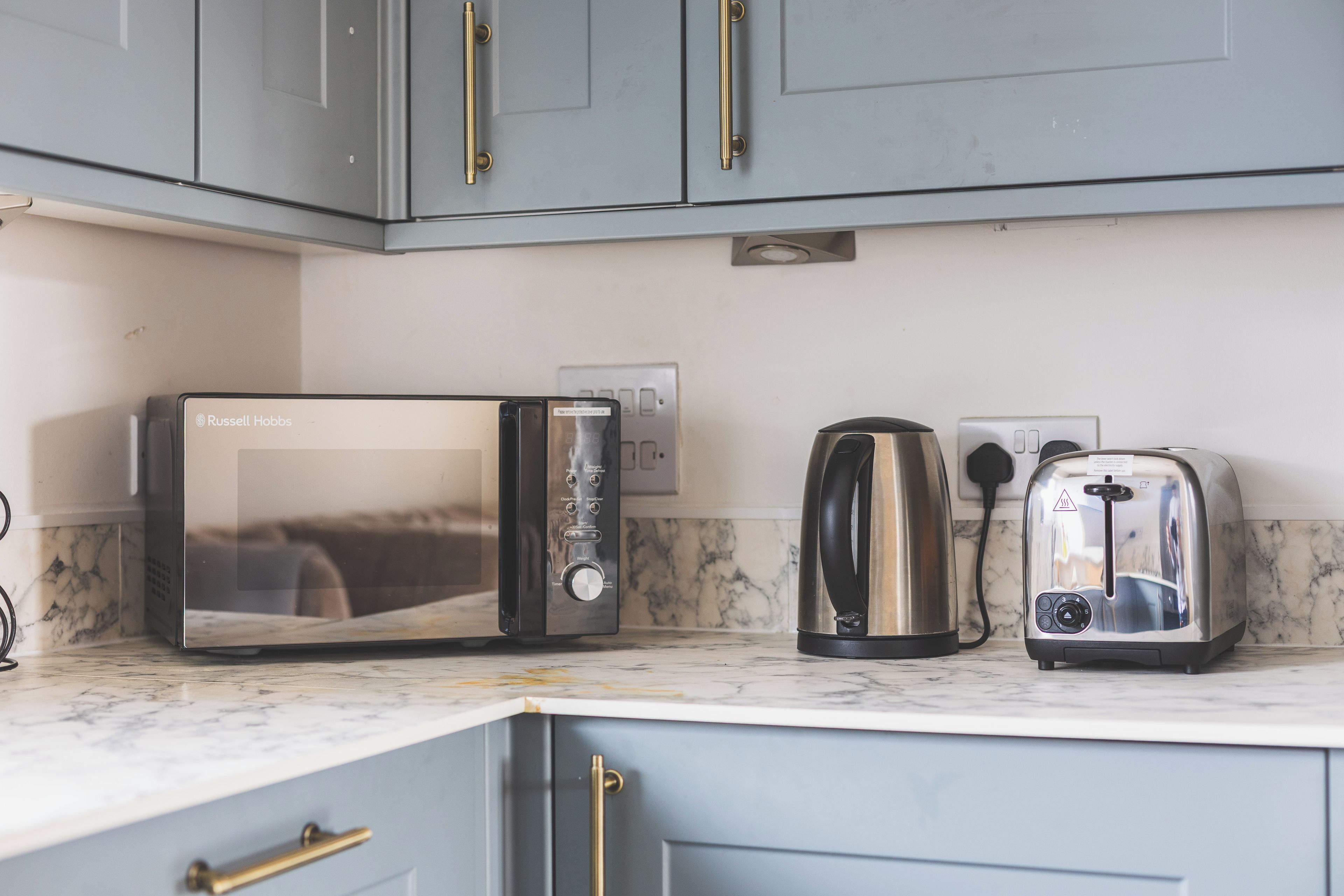 A kitchen with a built-in microwave, a kettle, and a toaster on a marble countertop.