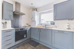 Een moderne keuken met grijze kastjes, een roestvrijstalen afzuigkap, een inbouwoven en een raam dat voor natuurlijk licht zorgt.