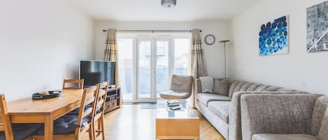 A living room with a sofa, a coffee table, a TV, and a dining area with chairs and a table.