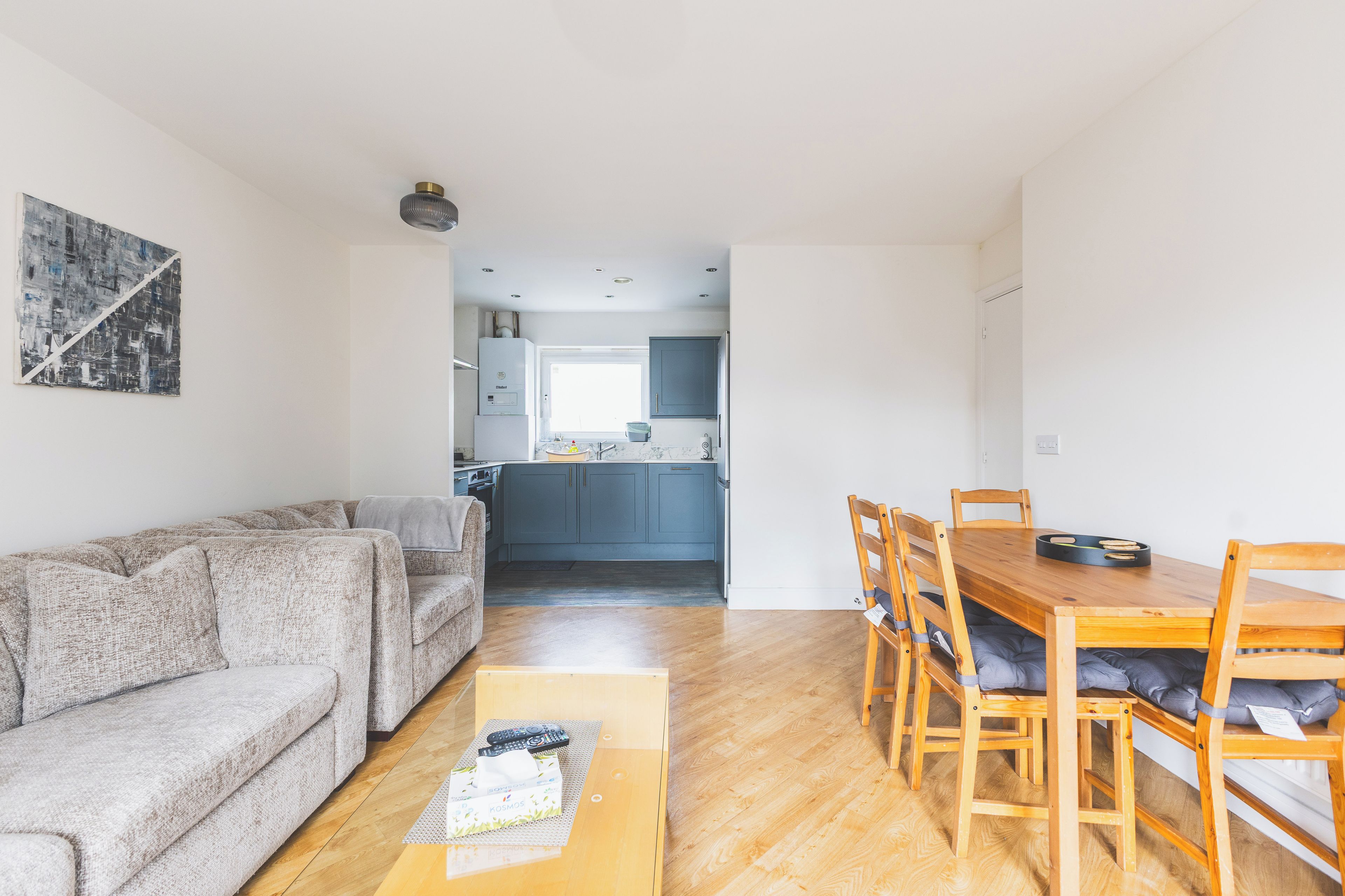 Un espacio habitable funcional con sofá, una mesa de comedor con sillas, una zona de cocina y un cuadro en la pared.