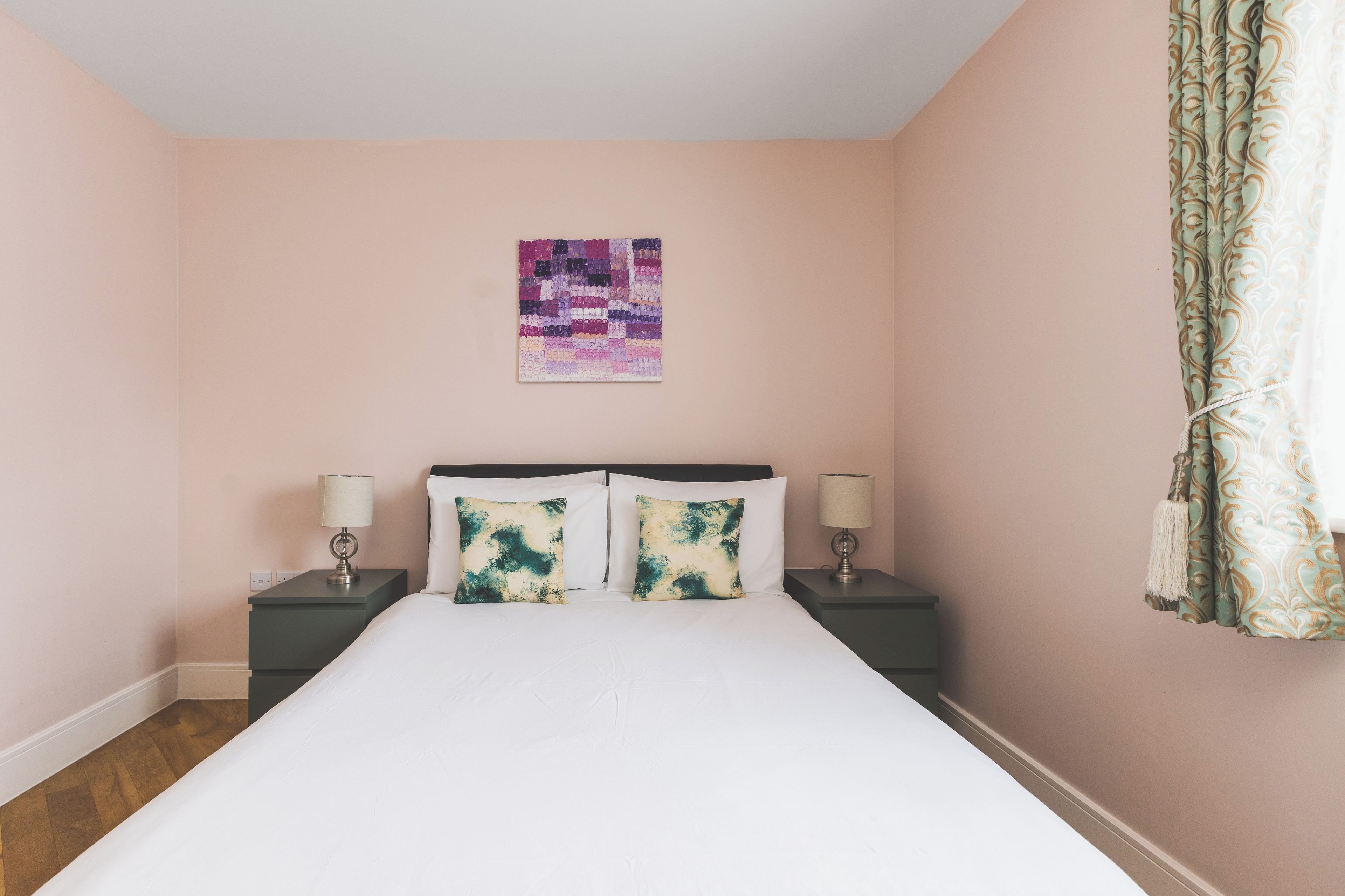 Un dormitorio con una cama, dos mesitas de noche, una lámpara de pared y una cortina estampada.