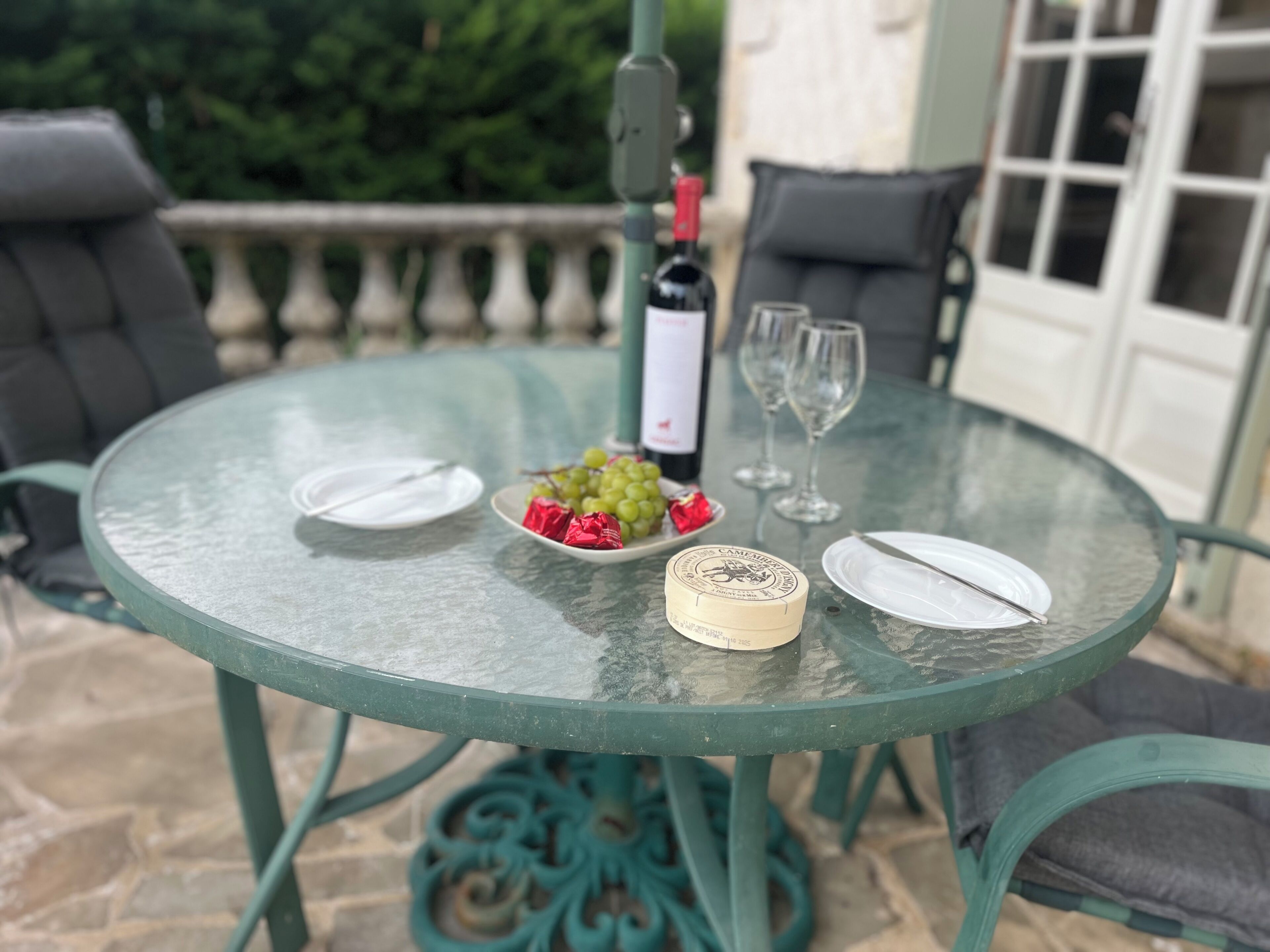 A round glass table with plates, a bottle, glasses, and a bowl of grapes.