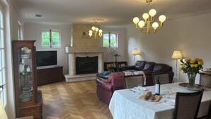 Ein großzügiges Wohnzimmer mit Kamin, Fernseher und einem Essbereich mit Tisch für zwei Personen.
