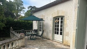 Eine Steinterrasse mit Tisch und Stühlen, einem grünen Sonnenschirm und einer weißen Tür mit Glasscheiben.