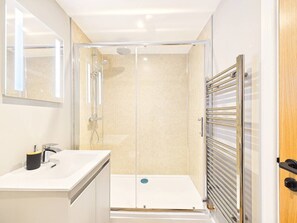 Un baño moderno con ducha de vidrio, un lavabo blanco con espejo y un perchero para toallas.