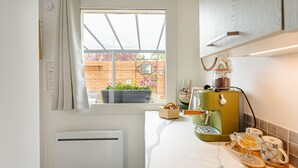 Une cuisine avec une fenêtre, un radiateur, une machine à café et un meuble en bois.