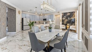 A modern kitchen with marble flooring, a dining area with a marble table, and a chandelier. - 355 Luxury House | Patio | GameRoom | Pool | Grill (Davenport)