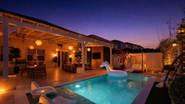 A swimming pool with a unicorn float, a covered patio area with tables and chairs, and a sunset sky. - 355 Luxury House | Patio | GameRoom | Pool | Grill (Davenport)