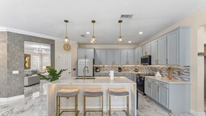 A modern kitchen with marble flooring, a central island with stools, and pendant lighting. - 355 Luxury House | Patio | GameRoom | Pool | Grill (Davenport)