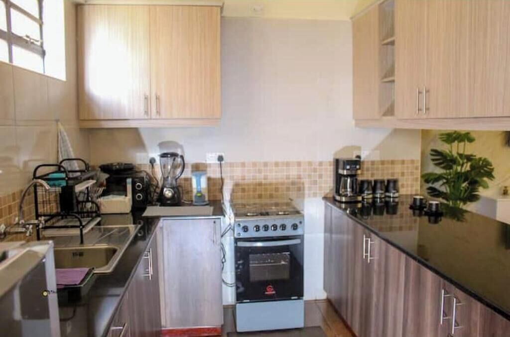 Een keuken met houten kastjes, een fornuis, een spoelbak en een koffiezetapparaat.