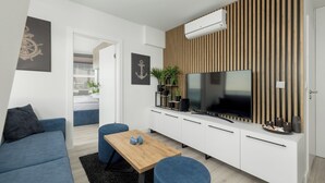 A modern living room with a sofa, a coffee table, a TV, and a wooden panel wall. - Serenity - Wave Resort & Spa (Międzyzdroje)