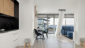 A modern apartment with a dining area, a living room with a blue sofa, and a balcony with a view. - Serenity - Wave Resort & Spa (Międzyzdroje)