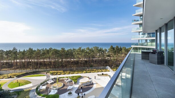 A modern building with a balcony overlooking a landscaped area and the sea. - Serenity - Wave Resort & Spa (Międzyzdroje)