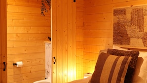 A wooden room with a bed, a door leading to a bathroom, and a wall-mounted artwork. - Luxury Wooden Wellness Forest House with Sauna -Amora 174 (Eindhoven)