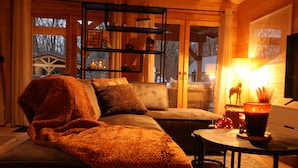 A cozy living room with a sofa, a coffee table, and a bookshelf. - Luxury Wooden Wellness Forest House with Sauna -Amora 174 (Eindhoven)