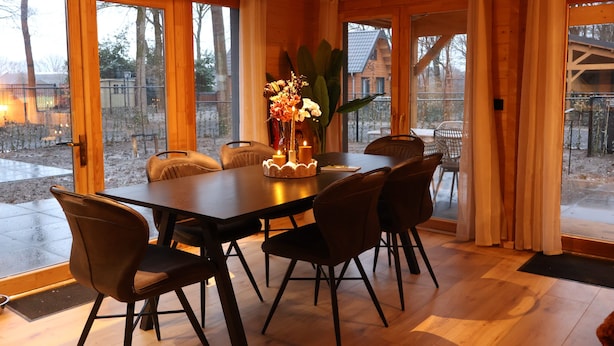 A dining area with a table, chairs, and a vase with flowers. - Luxury Wooden Wellness Forest House with Sauna -Amora 174 (Eindhoven)