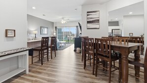 Een ruime eetruimte met een grote houten tafel en stoelen, een witte console tafel en uitzicht naar buiten.