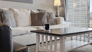 Een woonkamer met een bank, een salontafel, een lamp en een raam met zonwering.
