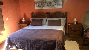 Une chambre à coucher avec un lit en bois, une table de chevet avec une lampe, un tableau accroché au mur et un plancher en bois.