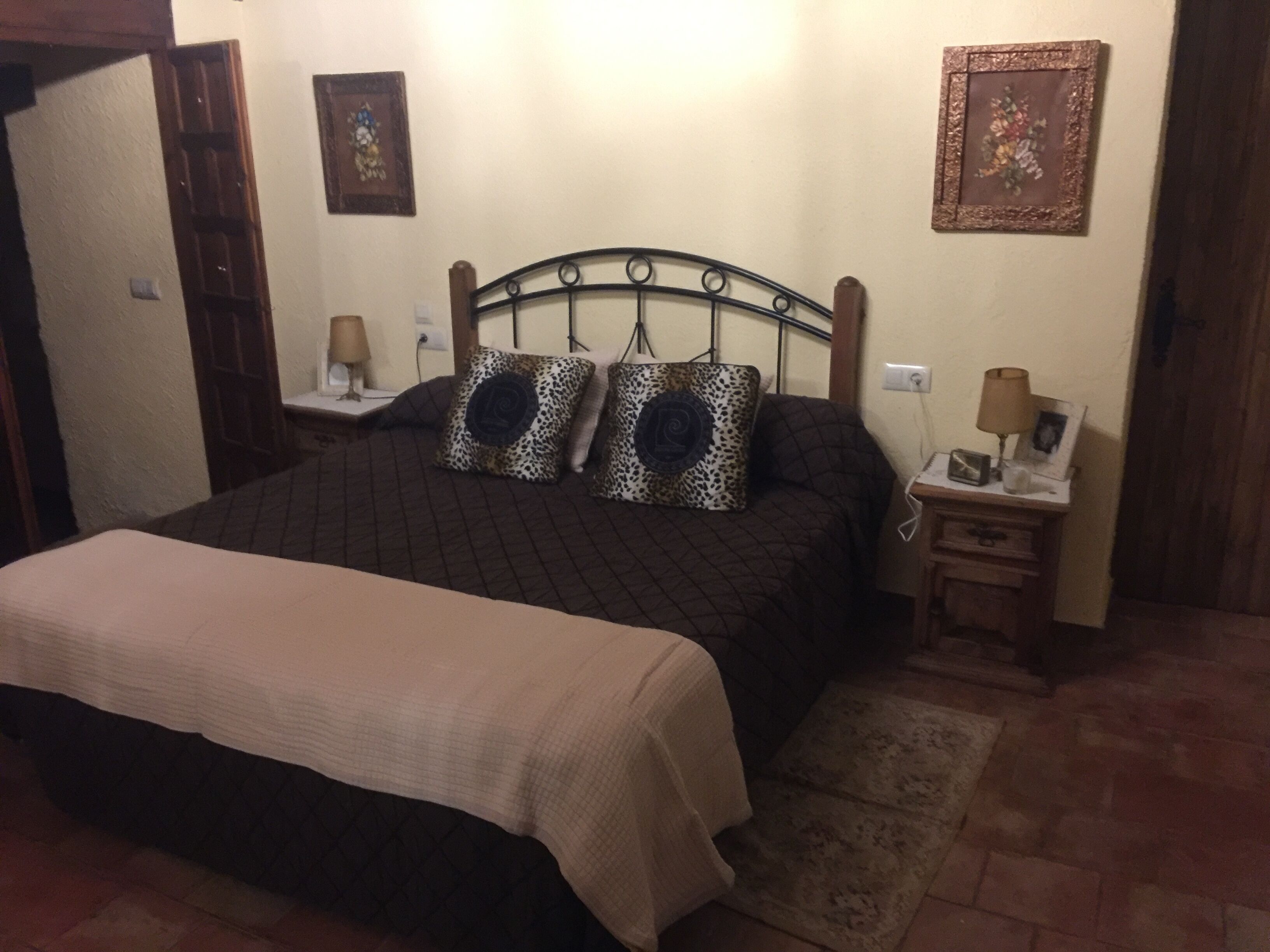 A bedroom with a bed, two bedside tables, a nightstand, a lamp, a rug, and a wall-mounted picture.