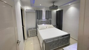 Un dormitori amb un llit, taules de nit, un ventilador de sostre i una unitat de climatització.
