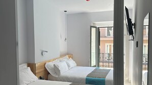 A hotel room with two beds, a balcony, and a view of buildings. - Hostal Palacio Leganitos (Madrid)