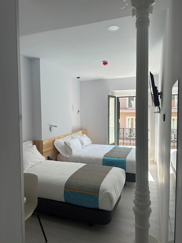 A hotel room with two beds, a balcony, and a view of buildings.