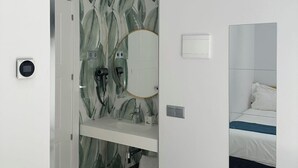 A bathroom with a shower, a sink, a mirror, and a bed in the adjacent room. - Hostal Palacio Leganitos (Madrid)