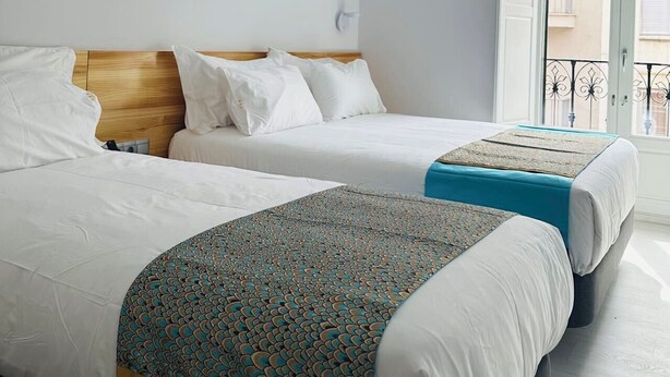 A hotel room with two beds, a wooden headboard, a balcony with a railing, and a door leading outside. - Hostal Palacio Leganitos (Madrid)