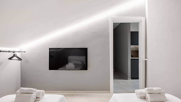 Een moderne hotelkamer met een groot bed, een kleiner bed, een flatscreen televisie aan de muur en een deur naar een gang.