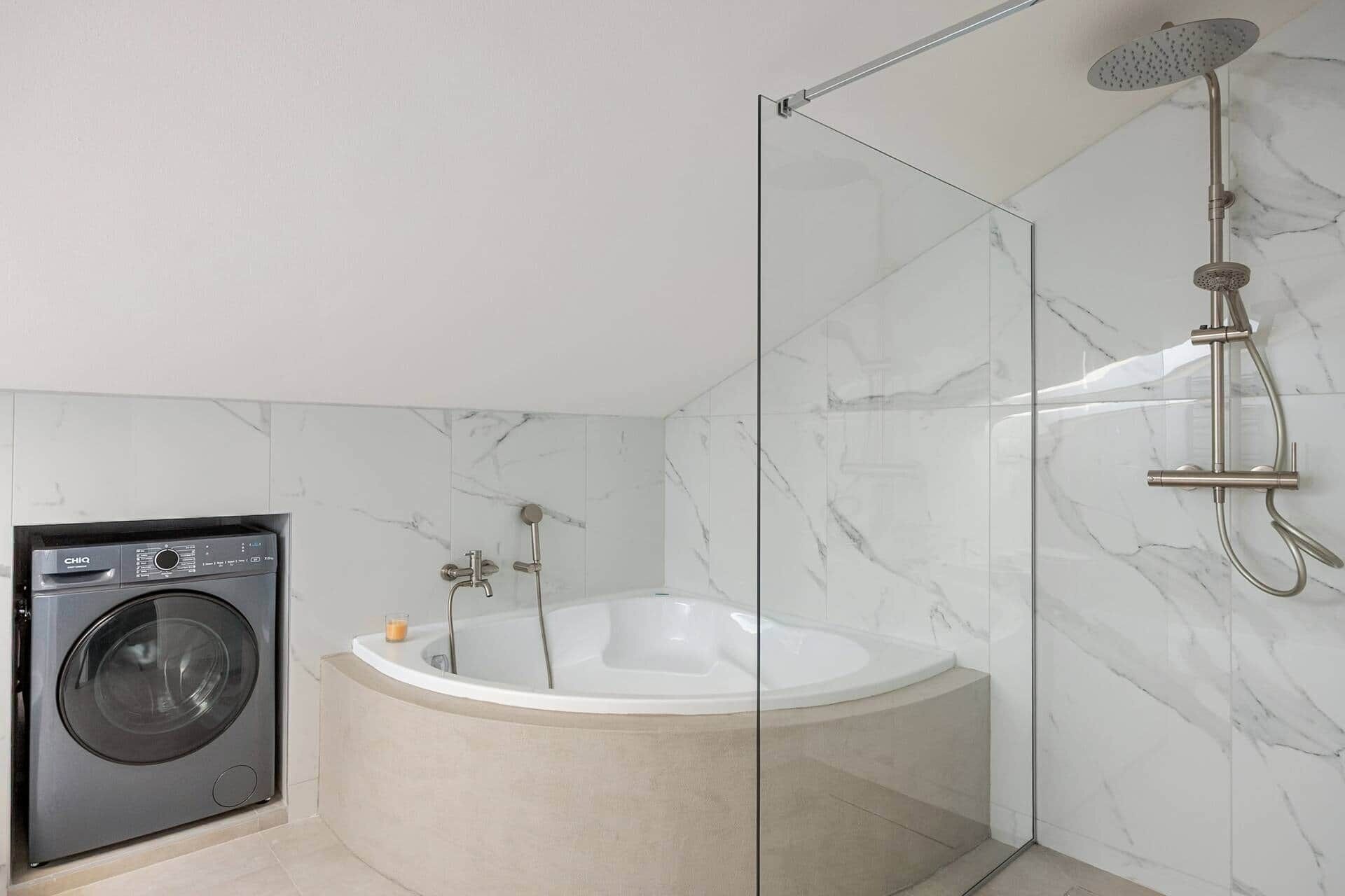 A modern bathroom with a glass-enclosed shower, a standalone bathtub, and a front-loading washing machine.