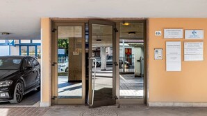 Een gevel met een draaideur, een geparkeerde auto en verschillende informatieborden aan de muur.