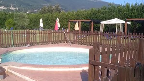 En swimmingpool med ett trästaket, en pergola och utsikt över berg i bakgrunden.