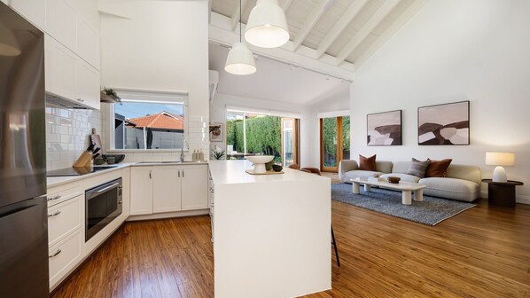 A modern kitchen with a central island, wooden flooring, and a dining area with a sofa and coffee table.